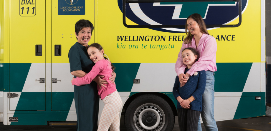 A smiling older woman hugs a young girl in pink while another smiilng woman and child look on