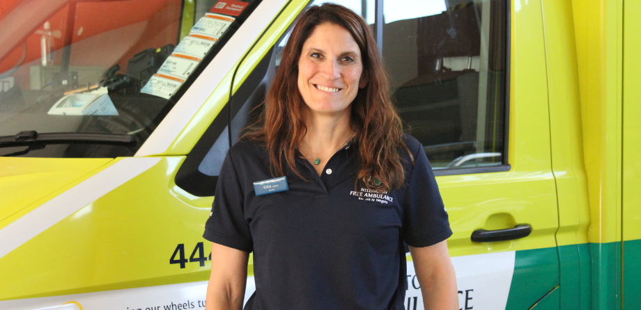 A woman with long brown hair smiles in front of an ambulance