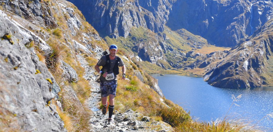 A man in running gear smiles as he runs along a stony path